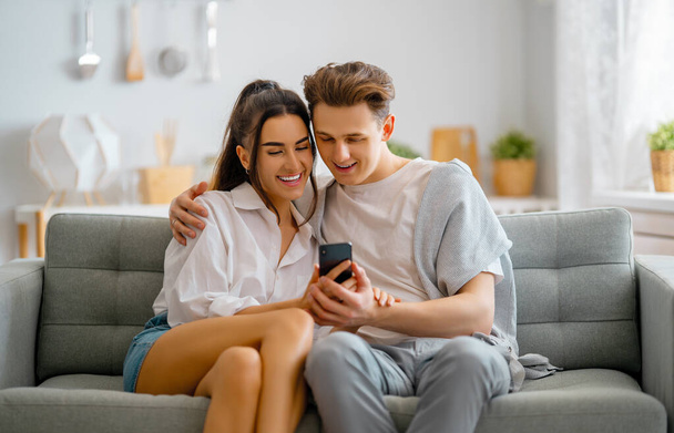 Young couple is using phones. Woman and man having fun staying at home. - Fotoğraf, Görsel