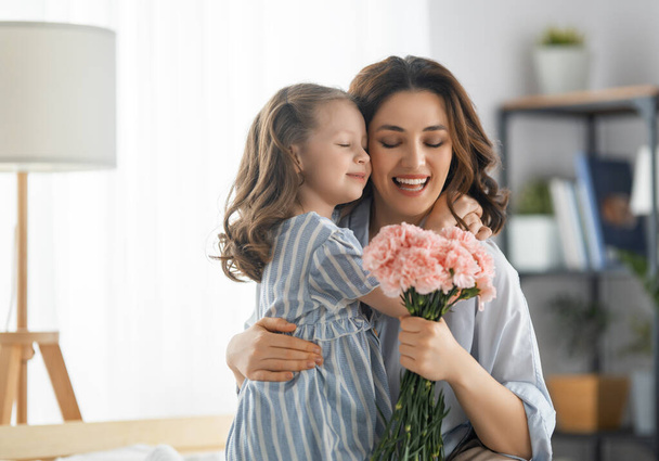 Guten Tag! Die Tochter gratuliert der Mutter und schenkt ihr Blumen. Mutter und Mädchen lächeln und umarmen sich. Familienurlaub und Zweisamkeit. - Foto, Bild