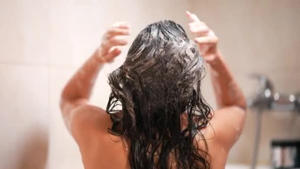 Nainen ottaa suihkun ja shampoot hiuksensa kylpyhuoneessa - Materiaali, video
