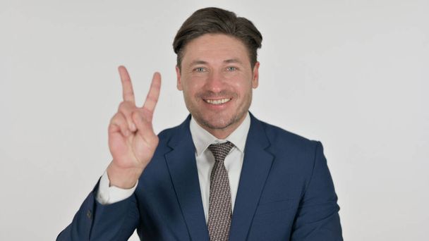 Uomo d'affari di mezza età che mostra il segno di vittoria con il dito, sfondo bianco - Foto, immagini