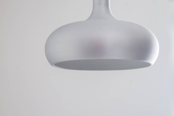 A silver metal lamp in a simple semicircular shape hangs on the ceiling against a gray wall background - Valokuva, kuva