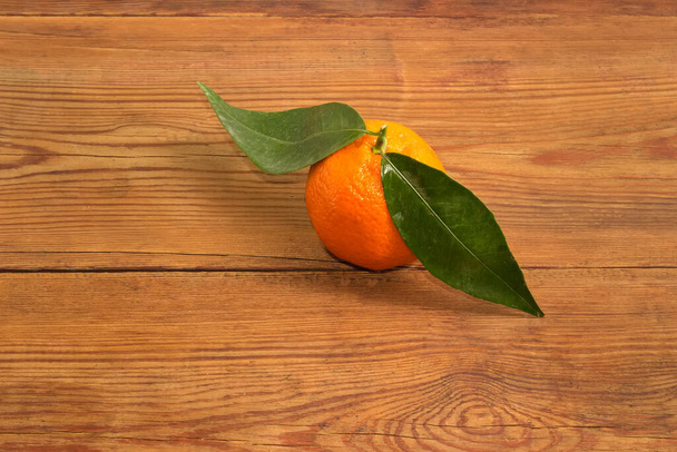 Single tangerine on a small twig with leaves on the old rustic table - Fotó, kép