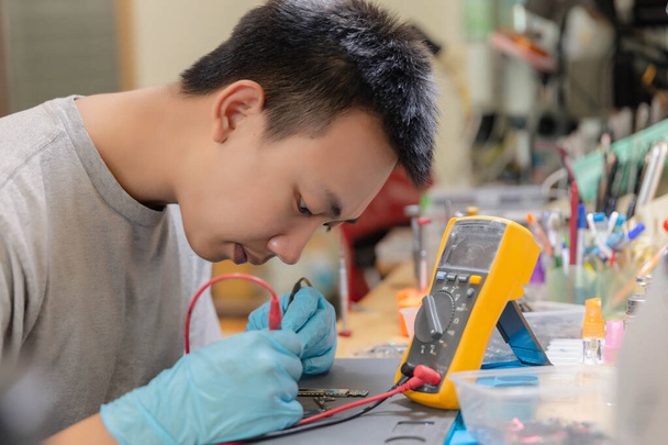 Concept de réparation de téléphone un jeune technicien électrique utilisant un ampèremètre mesurant le courant dans un circuit d'un appareil électronique. - Photo, image