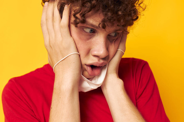 portrait of a young curly man in a red t-shirt medical mask protection yellow background unaltered - Fotografie, Obrázek
