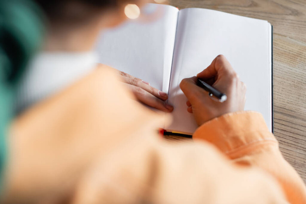 vista ritagliata di scrittura studente offuscata su notebook vuoto a casa - Foto, immagini