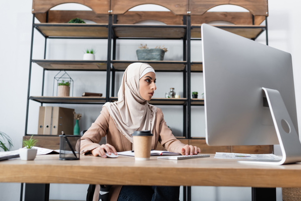 Ofiste bilgisayarın yanındaki bulanık rafta çalışan Arap iş kadını. - Fotoğraf, Görsel