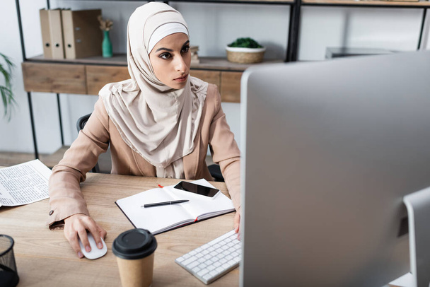 arabian businesswoman looking at computer monitor near notebook and cellphone with blank screen - Valokuva, kuva