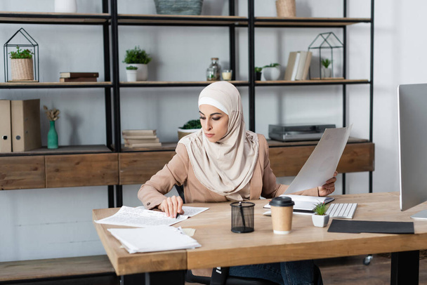 jeune femme arabe travaillant avec des journaux et des documents près de l'écran d'ordinateur à la maison - Photo, image