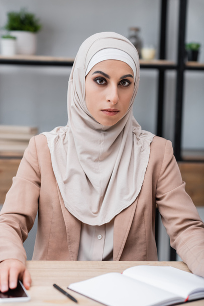 muzułmanka w hidżabie siedzi obok pustego notebooka i telefonu komórkowego w domu - Zdjęcie, obraz