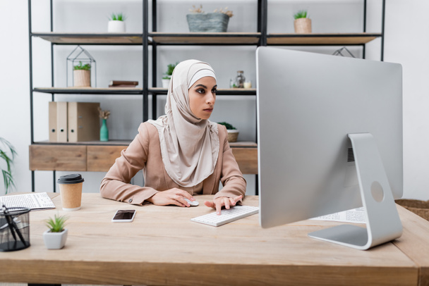 young muslim woman working on computer near smartphone with blank screen and coffee to go - Fotoğraf, Görsel
