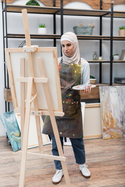 pełny widok długości muzułmanki malowanie na sztalugach w domu studio - Zdjęcie, obraz