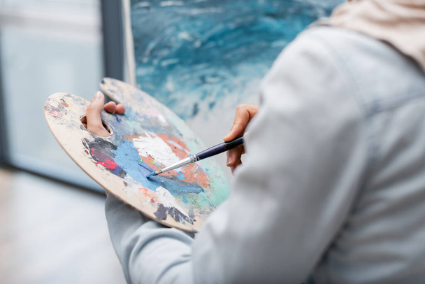 partial view of woman with paintbrush near blurred picture - Foto, imagen