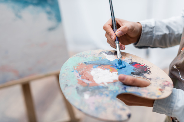 partial view of artist mixing oil paints on palette on blurred background - Fotoğraf, Görsel