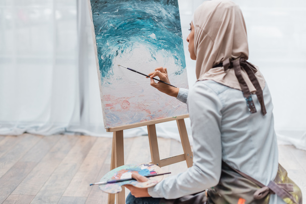fiatal muszlim nő hidzsáb festés festőállvány otthon - Fotó, kép