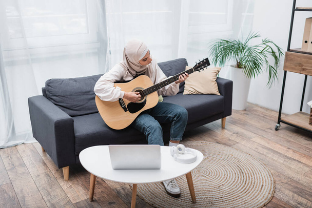 arabian woman playing guitar during video lesson on laptop at home - Fotó, kép
