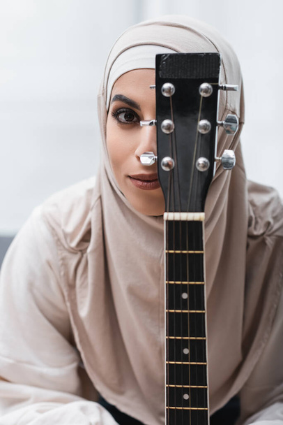 arabian woman in hijab looking at camera near guitar neck - Фото, изображение