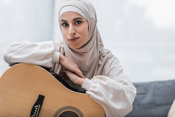 young muslim woman looking at camera near acoustic guitar - Fotoğraf, Görsel