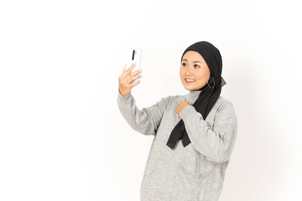 Videollamada con smartphone de la hermosa mujer asiática con Hijab aislado sobre fondo blanco - Foto, Imagen