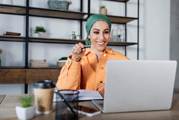 alegre mujer musulmana señalando a la computadora portátil durante la lección en línea en casa - Foto, Imagen