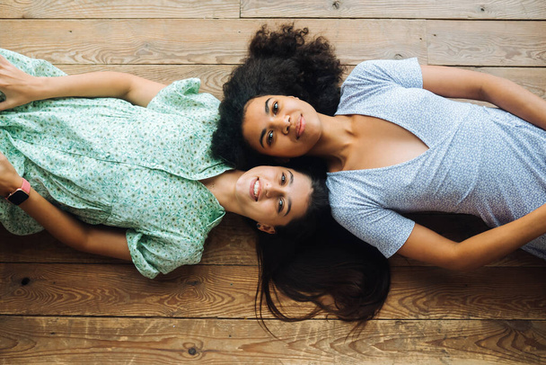 Δύο νέες γυναίκες ξαπλώνουν πρόσωπο με πρόσωπο στο πάτωμα. - Φωτογραφία, εικόνα