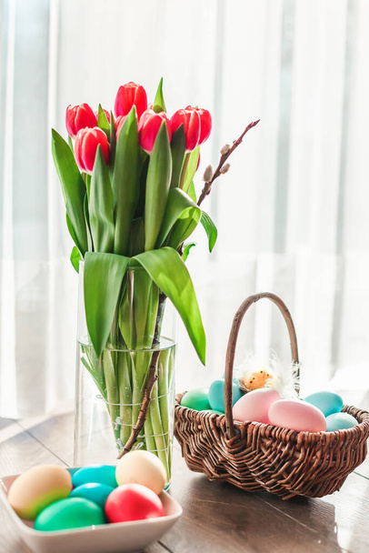 Pastel colored Easter eggs in a basket with red tulips in a vase - Fotografie, Obrázek