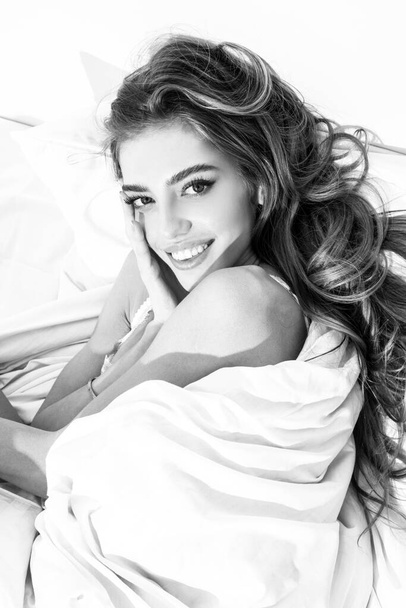 Smiling sensual woman laying in bed under a duvet in bedroom. Good morning. - Photo, Image