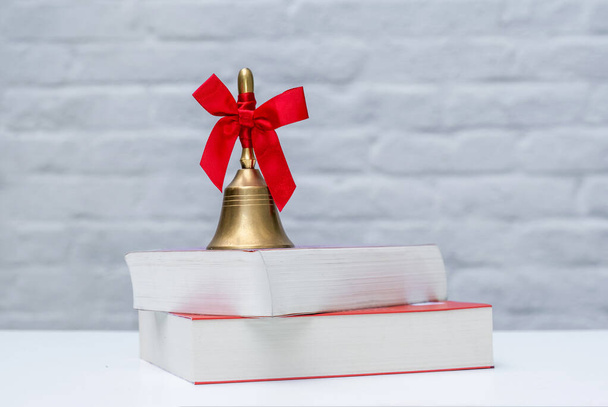 Золотий дзвін з червоною стрічкою залишається на двох книгах на білому тлі, шкільної концепції. - Фото, зображення