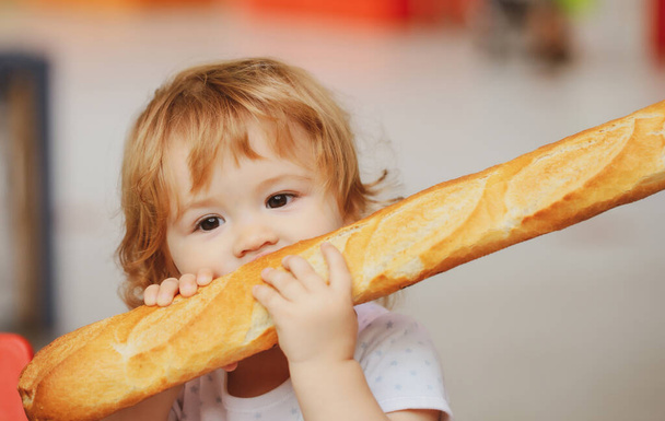 Cute baby eating French baguette white bread. Funny toddler child eating sandwich, self feeding concept. - Foto, Imagen
