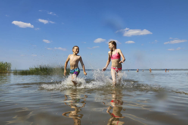 Ein Junge und ein Mädchen spielen im Sommer gemeinsam im See. - Foto, Bild