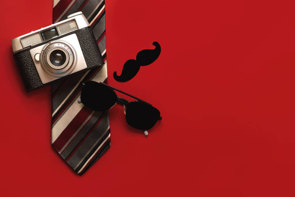 Happy Father's Day. Top view of tie, false mustache,sunglasses and retro photo camera with copy space over red background. Father's Day celebration concept - Photo, Image