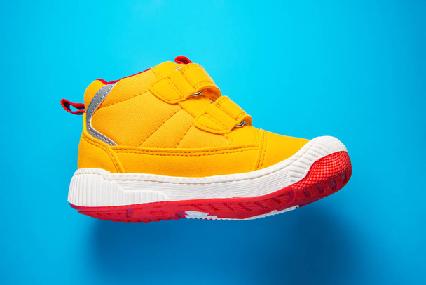 Gele baby schoenen. Kids sport sneakers geïsoleerd op blauwe achtergrond - Foto, afbeelding
