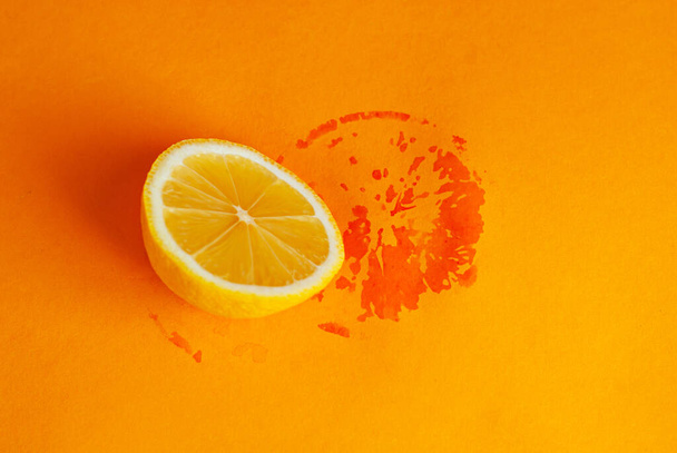 Half a lemon on an orange background. Wet imprint of lemon on paper. - Фото, изображение