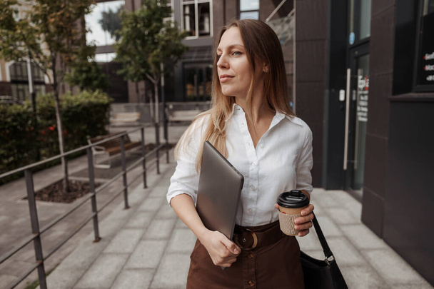 Fechar retrato mulher de negócios segurando café e laptop do fundo do edifício  - Foto, Imagem