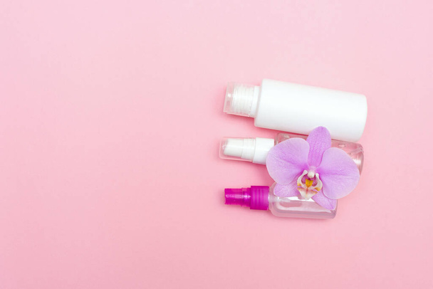 flache Liege mit Kosmetikflaschen und Orchideenblume auf rosa Hintergrund mit Kopierraum für Text. Cremegläser Set von oben. Das Konzept der Gesichts- und Körperpflege. - Foto, Bild