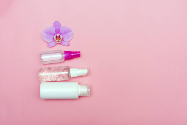 flache Liege mit Kosmetikflaschen und Orchideenblume auf rosa Hintergrund mit Kopierraum für Text. Cremegläser Set von oben. Das Konzept der Gesichts- und Körperpflege. Gesichtspflege - Foto, Bild
