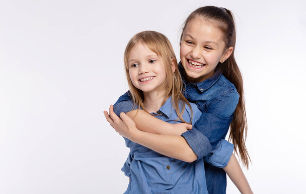 二人の幸せな友人や姉妹の子供の女の子抱擁。白を背景に楽しさと感情を持ち、笑顔で、友情と関係のライフスタイルの人々のコンセプト - 写真・画像