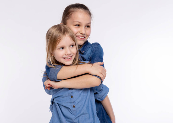 Двоє щасливих друзів або сестер, які обіймають дівчаток. Разом розважатися і позувати емоції на білому тлі, щасливі усміхнені, дружба і спосіб життя людей концепція
 - Фото, зображення