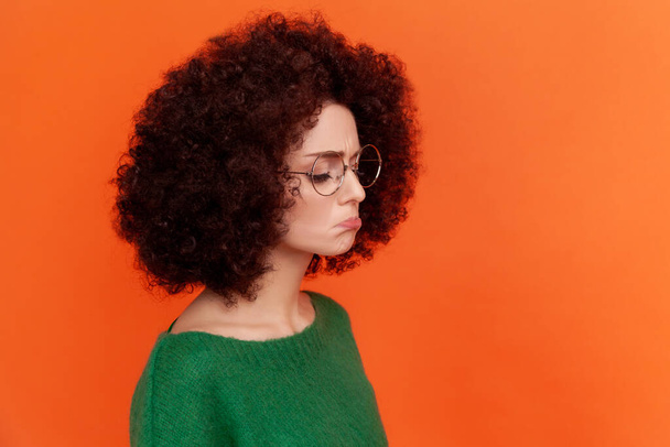 Profile portrait of sad upset woman with Afro hairstyle wearing green casual style sweater standing with pout lips, feels sadness, cry. Indoor studio shot isolated on orange background. - Fotografie, Obrázek