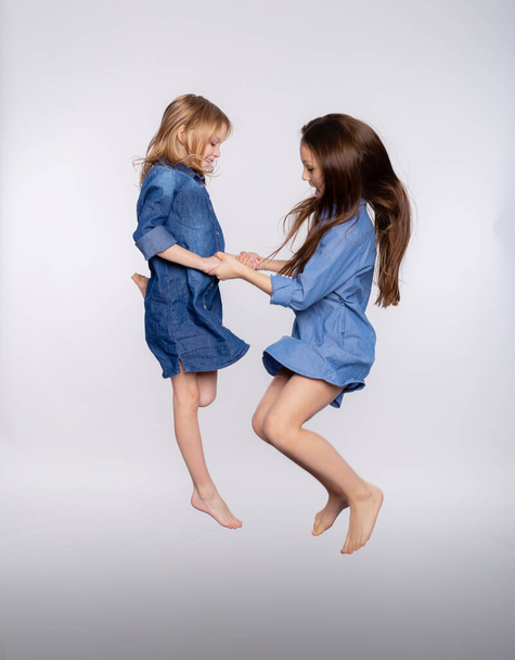 Full size portrait of two excited cute children girls enjoy jumping open mouth isolated on gray background. Loving sisters or friends jumping up playing and having fun - Photo, Image
