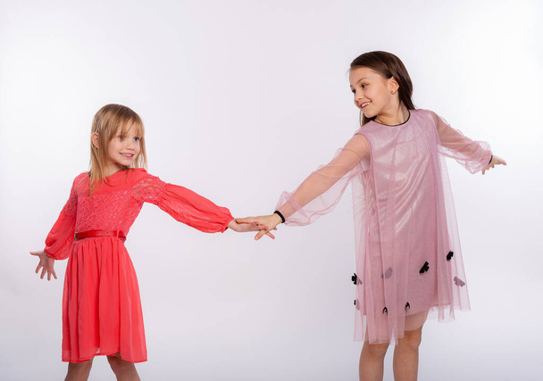 Miúdos divertidos, conceito divertido. Retrato de duas meninas bonitos 6-8 anos de idade vestindo vestido rosa e dançando isolado no fundo branco. Dia das Mães, família do amor, conceito da infância da paternidade - Foto, Imagem