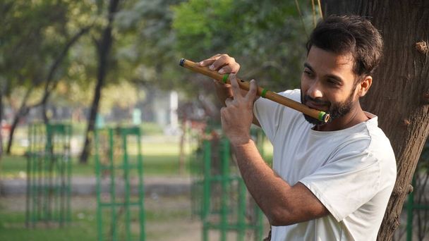 Bansuri speler speelt muziek in zonneschijn in Park - Indian Flute Player - Foto, afbeelding
