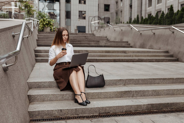 Junge Geschäftsfrau hält Kaffee und arbeitet mit Laptop auf der Straße der Stadt - Foto, Bild