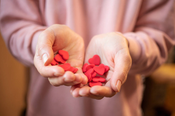 Hands holding red valentines on valentine's day. The girl's hands hold a lot of small hearts and fast-setting plasticine. The 14th of February. Holiday of love. The concept of giving love - Fotografie, Obrázek