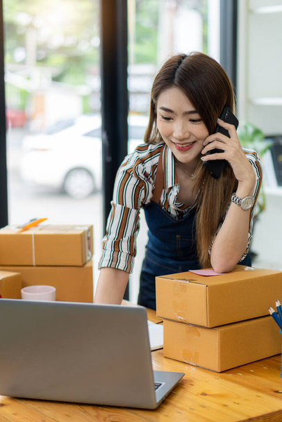 Kisvállalkozás indítása, kkv, független vállalkozó ázsiai nő otthon dolgozik kartondobozok, okostelefonok, laptopok, online, marketing, csomagolás, szállítás, kkv, e-kereskedelmi koncepció. - Fotó, kép