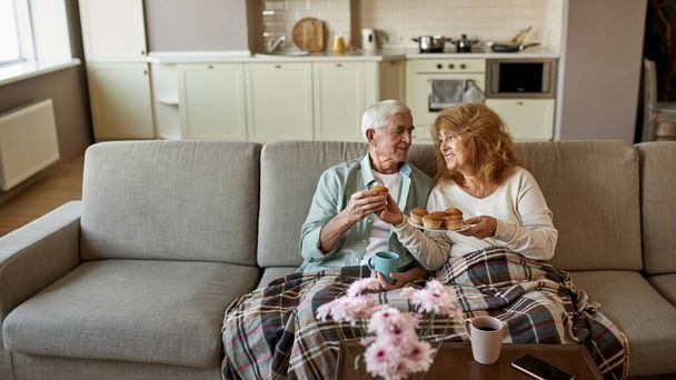 Женщина дарит кекс мужу с чашкой на диване - Фото, изображение