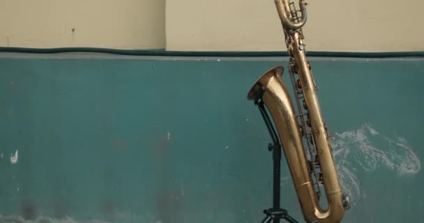 Duży saksofon stoi na podstawce na tle starej, brudnej ściany - Materiał filmowy, wideo