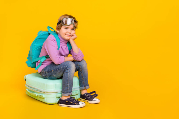 Full size photo of funny relaxing boy sitting on baggage go on adventure trip isolated on yellow color background. - Фото, зображення