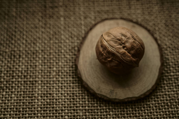 Rounded walnut  on a burlap on a brown burlap (top view). Unpeeled walnut in a shell on a sackcloth - Фото, изображение