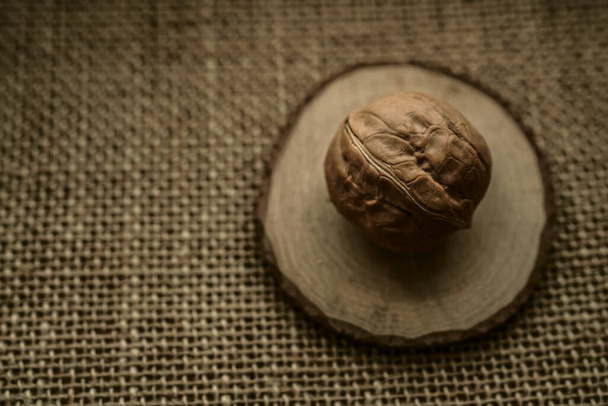 Rounded walnut  on a burlap on a brown burlap (top view). Unpeeled walnut in a shell on a sackcloth - Foto, Bild