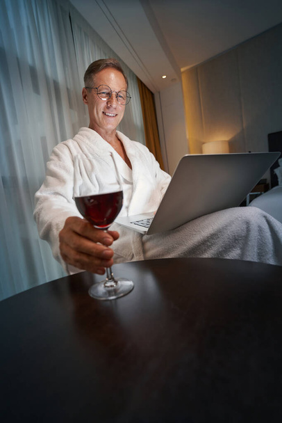 Freundlicher Mann entspannt sich mit Wein und erledigt einige Arbeiten - Foto, Bild
